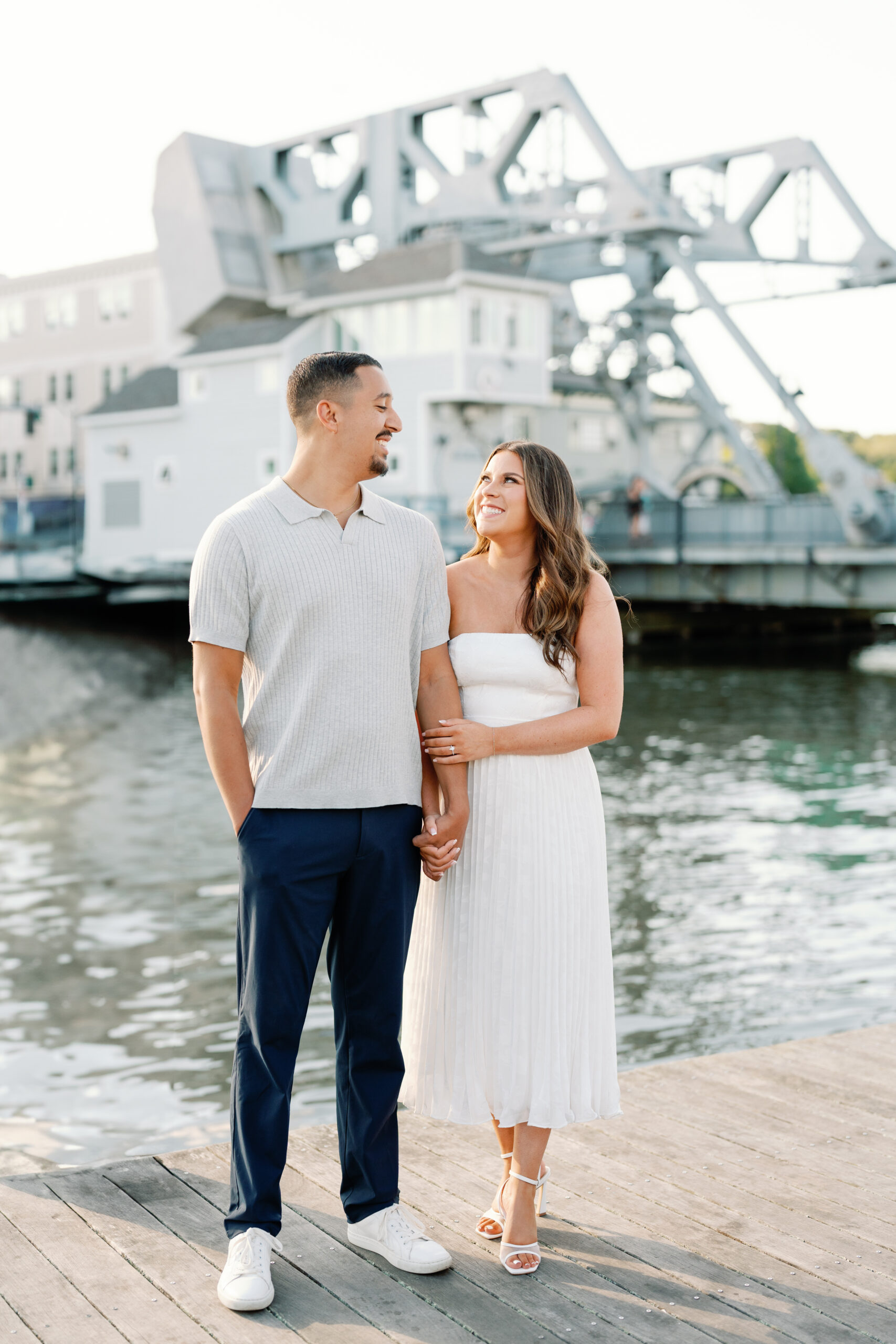 Engaged couple laughing together in downtown Mystic, Connecticut with coastal New England scenery and warm summer light