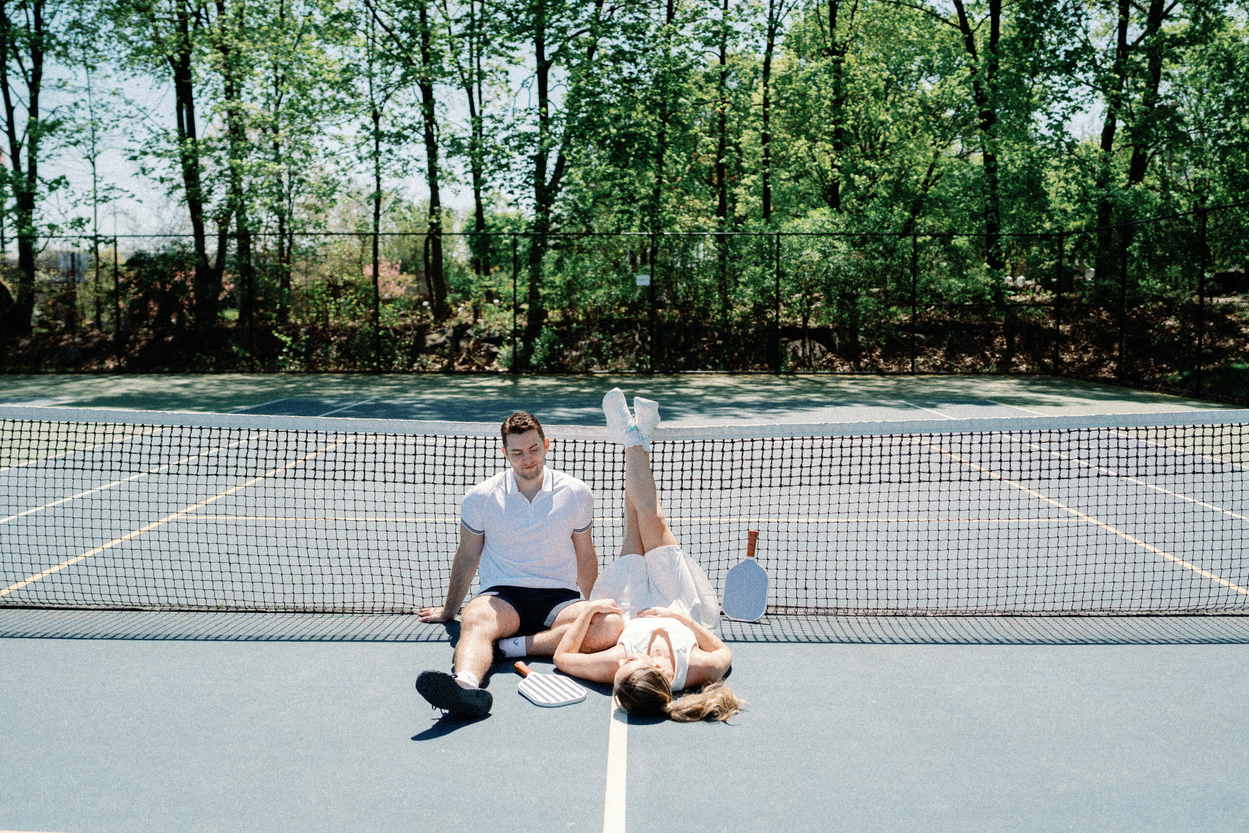 Close up engagement photo of couple holding pickleball paddles and laughing on court, Norwalk CT